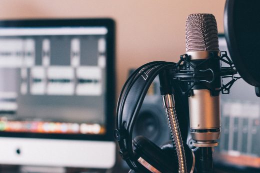 photograph of a microphone and headset in the front and a computer screen that shows some audio tracks in the blurred background